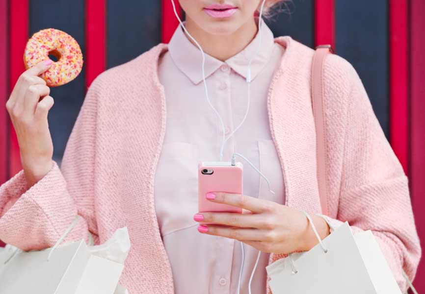 Woman wearing all pink, holding her phone in one hand and a doughnut in the other